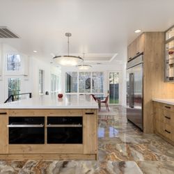 AGC Home Remodeling - Open kitchen with Euro-style cabinets, double ovens, display shelves, and bold porcelain tile in a luxury Austin home.