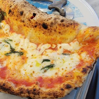Nella Pizza e Pasta - Mezza Luna - $22 as of 8/2023 - A slice of Neapolitan pizza with melted cheese, tomato sauce, and basil leaves on a marble table surface. - Pizza Near Me - Chicago, Illinois