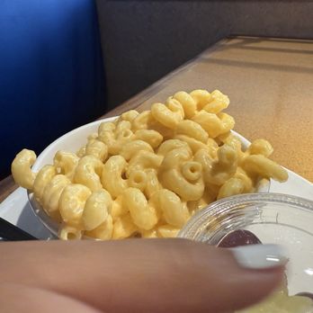 Wildflower - Kids Mac and cheese which has a side of fruit a cookie and a drink for a reasonable amount of money. - A bowl of macaroni and cheese with a creamy cheese sauce is placed on a restaurant table. Next to it, there is a clear plastic container with a fruit side, a cookie, and a drink. The setting appears to be a casual dining environment, possibly a health-conscious eatery. - Sandwiches Near Me - Chandler, Arizona
