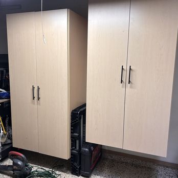 CD Kitchen & Bath Remodel - Excellent and beautiful storage! - Two light wood-finish storage cabinets are mounted on a wall in a workshop or garage setting, with tools and equipment nearby. - General Contractors Near Me