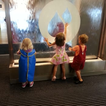 Thinkery - Kids playing along a water wall. Picture of the apron that helps protect clothes from getting too wet - Kids Activities Near Me - Austin, Texas Thinkery - Kids playing along a water wall. Picture of the apron that helps protect clothes from getting too wet - Kids Activities Near Me - Austin, Texas