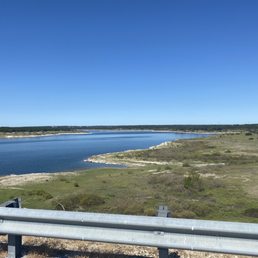 A scenic view of Lake Georgetown with calm water, grassy shores, and a bright blue sky, captured from a roadside vantage point.