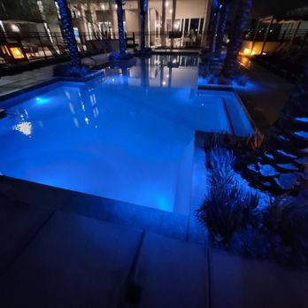 AVE Phoenix Terra - A swimming pool illuminated with blue lights at night, surrounded by palm trees and outdoor seating areas, in a residential complex. - Apartments Near Me - Phoenix, Arizona