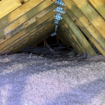 Cool Spaces Insulation - The end result is a satisfying and money saving layer of insulation in the attic and over the garage. - The photo depicts an attic space with wooden roof trusses arranged in a triangular pattern. The roof structure is supported by wooden beams, some of which have metal plates at the joints. The floor is covered with pink insulation material, and the space appears to be unfinished. The image provides a clear view of the attic's structural elements and insulation. - Insulation Installation Near Me