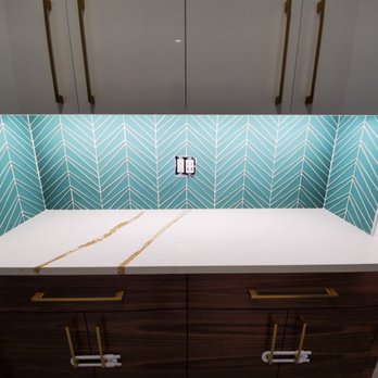 RAPHA'S TILE - a kitchen countertop with a window - A kitchen countertop features a blue and white geometric backsplash with a central electrical outlet, surrounded by dark wood cabinets. - Flooring Near Me