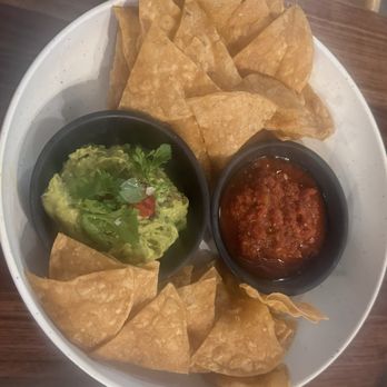 Hidden Creek Estates - Guacamole and Chips - Tortilla chips are arranged around two small black bowls containing guacamole and salsa, on a white plate. - Venues & Event Spaces Near Me - Roscoe, Illinois