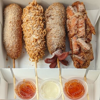 Chungchun Rice Dogs - Original, ramen chip, squid ink cheese, and sweet potato hot dogs with sweet garlic on top. Sweet chili and sweet mayo sauces. - Korean Near Me - Aurora, Ontario