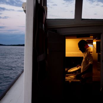Casco Bay Custom Charters - Private chef highlighted in preparing food against a darkening sky in Casco Bay. - Boat Charters Near Me - Portland, Maine