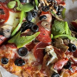 A pizza with toppings including black olives, green peppers, mushrooms, pepperoni, and melted cheese, served on a pizza tray.