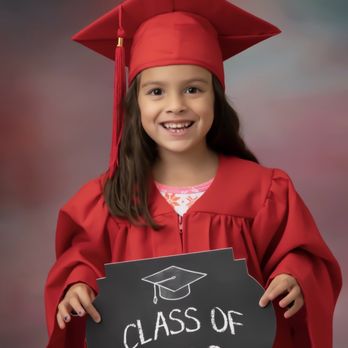 Children's Lighthouse of Cedar Park - Brushy Creek - School Graduation Photos Pre-K Grads - A girl in a red graduation cap and gown holds a sign that says 'Class of 2022,' smiling at the camera. - Preschools Near Me - Cedar Park, Texas