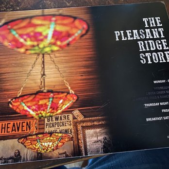 Pleasant Ridge Store - Back of the menu - The Pleasant Ridge Store menu displays its weekly schedule, including closing on Mondays, special events on Wednesday and Thursday nights, and breakfast hours on Saturday. The background features colorful stained glass lamps hanging from the ceiling, with a partial view of the store interior and signage. The photo credit is given to Josh Demuth. - Bars Near Me - Dodgeville, Wisconsin