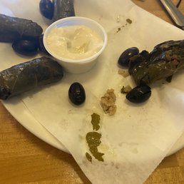 a plate of stuffed grape rolls, olives, and dipping sauce