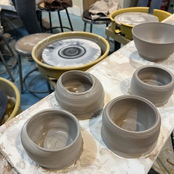 Choplet - Several unglazed ceramic bowls are arranged on a worktable in a ceramic studio. The bowls are in various stages of shaping, with some appearing more rounded and smooth. In the background, pottery wheels, stools, and other studio equipment are visible, indicating an active workspace for pottery making. - Art Schools Near Me - Brooklyn, New York