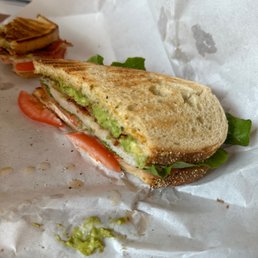BLTT (with added avocado) - A toasted sandwich with tomato slices, lettuce, and avocado spread on white bread, partially eaten and placed on white paper.