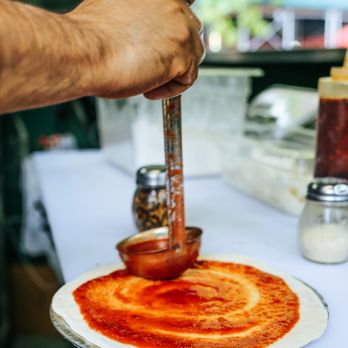 Sfila Pizza - a person spreading sauce on a pizza - Pizza Near Me - New York, New York Sfila Pizza - a person spreading sauce on a pizza - Pizza Near Me - New York, New York