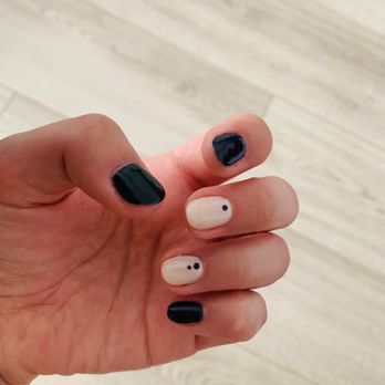 Starlight Nails - Gel manicure - Hand with manicured nails, some painted black and others white with small black dots, against a light wooden background. - Nail Salons Near Me - Arlington, Virginia