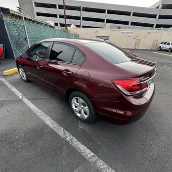 Rulis Window Tinting - A maroon Honda Civic is parked in a marked parking space in an outdoor lot, with a fence and a building with a 'RIM REPAIR' sign in the background. - Car Window Tinting Near Me - Phoenix, Arizona