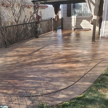 Gumer Concrete LLC - A stamped concrete patio is shown, wet and shiny, with a metal railing along the edge and a house with siding and curtains in the background. - Masonry/Concrete Near Me - Denver, Colorado