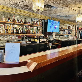 Maharaja - a view of a bar with a television on the wall - A bar interior featuring shelves stocked with liquor bottles, glassware, and a mounted TV screen, with a wooden bar counter. - Indian Near Me - Milwaukee, Wisconsin