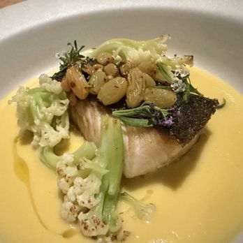 Tavernetta - A plated dish includes a piece of cooked fish with crispy skin, surrounded by cauliflower and broccoli florets, topped with nuts and herbs, and served on a yellow sauce. The presentation emphasizes fresh ingredients and careful plating. - Italian Near Me - Denver, Colorado