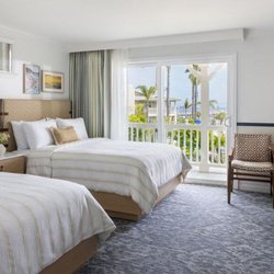 Renovated guest suite with two queen beds, bright white linens, blue accent trim, and outdoor balcony access.