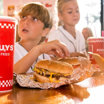 Five Guys - A red Five Guys soft drink cup is the focus in the foreground, as children enjoy their meals in the background. - Hot Dogs Near Me - Newton, New Jersey