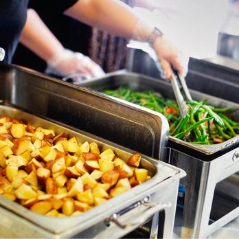 Catering Concepts - Trays of cooked potatoes and green vegetables are displayed at a catering setup, with staff serving food. - Party & Event Planning Near Me - Lowell, Arkansas