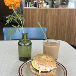 The Coffee Shop by Hammerhead Coffee Roasters - Breakfast sandwich and a pumpkin spice slushy on a table with a flower on it and the coffee counter in the background.