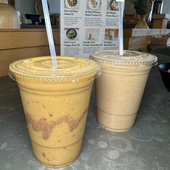 Organic Krush Kitchen & Eatery - Two smoothies in clear plastic cups with straws are placed on a table at a cafe, with a menu featuring fall-themed dishes in the background. - Juice Bars & Smoothies Near Me - Plainview, New York