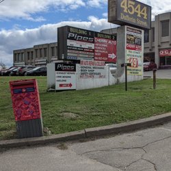 Ocak Basi - From the sidewalk looking at the restaurant front the driveway where there's a sign with the restaurant's name & phone number. May 2021