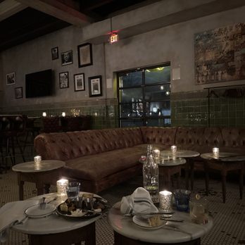Eberly - Inside - A restaurant interior features a large brown leather sectional sofa, small tables with candles, and a wall decorated with framed photos and artwork. - Bars Near Me - Austin, Texas