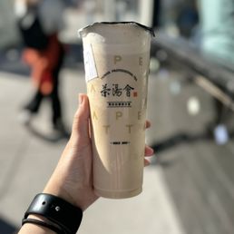 Tie Guan Yin Milk Tea - A person holds a tall cup of Taiwan milk tea with a plastic lid, with a blurred street scene in the background.