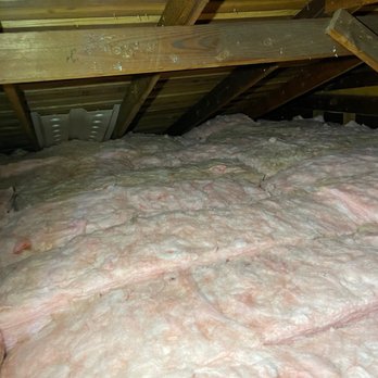 Johnson's Insulation - The image shows an attic space with visible wooden rafters and beams. The floor is covered with pink fiberglass insulation, which is used for thermal insulation in residential buildings. The insulation appears to be spread across the attic floor, and the space is enclosed by the roof structure. There are no other objects or features visible in the attic. - Insulation Installation Near Me - Oakland, California