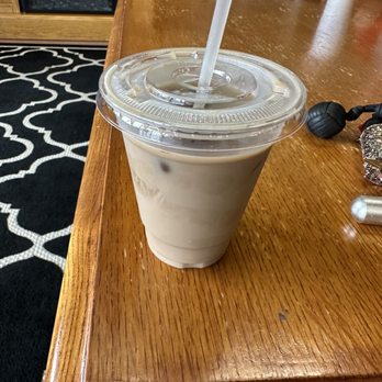Bittersweet Java - Ice vanilla latte - A clear plastic cup filled with iced vanilla latte, topped with a plastic lid and straw, placed on a wooden table in a coffee shop. - Coffee & Tea Near Me - Ruckersville, Virginia