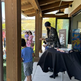 Amasingh Magic - A magician in a floral jacket entertains children outdoors near a building with a wooden roof structure. - Magicians Near Me
