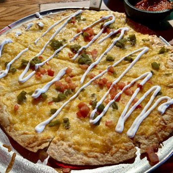 Aunt Chilada's - Cheese Crisp - A cheese crisp pizza with melted cheese, diced tomatoes, green peppers, and sour cream drizzle, served on a metal tray at a Mexican restaurant. - Mexican Near Me - Tempe, Arizona