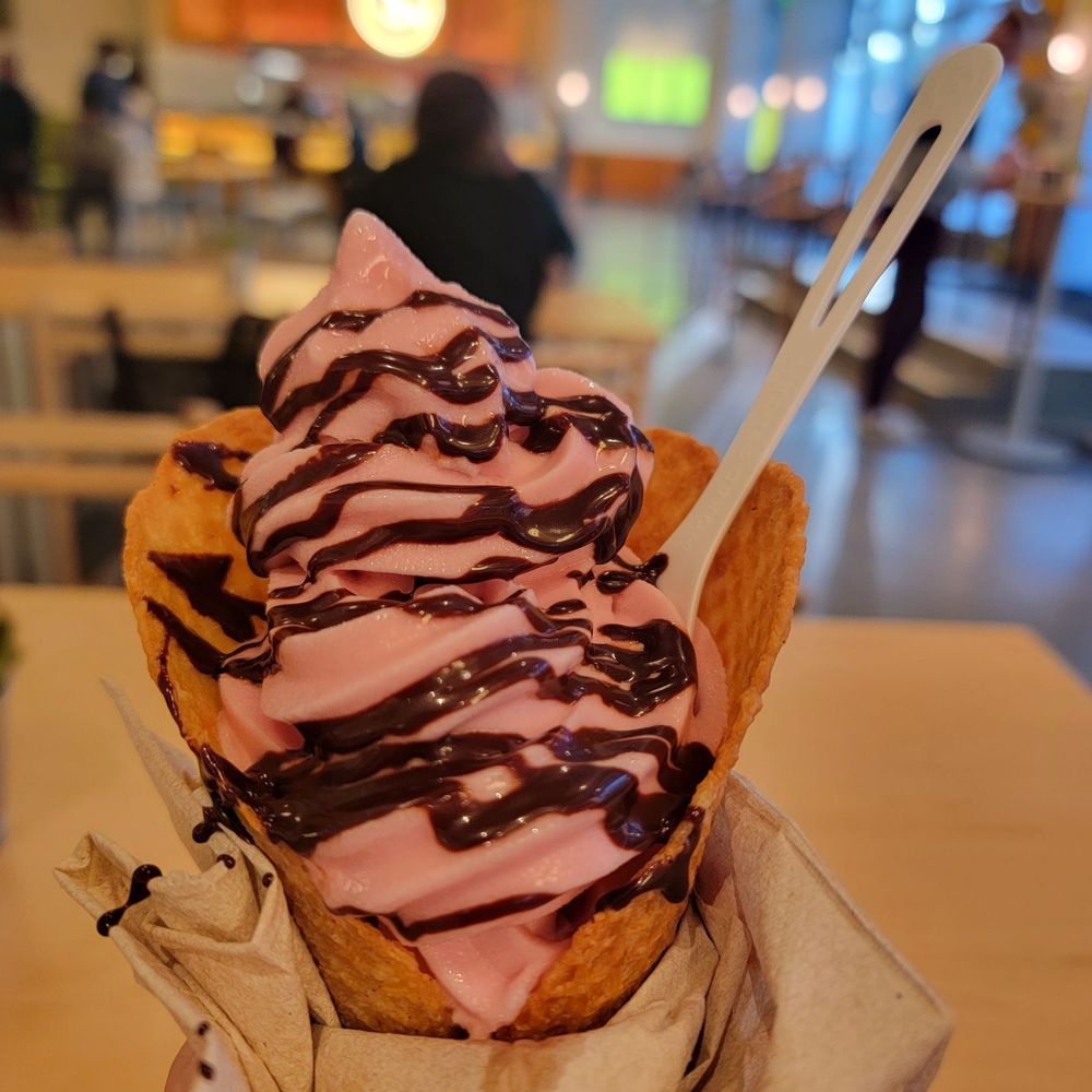 Strawberry plant based soft serve with chocolate syrup in a freshly made waffle cone Strawberry plant based soft serve with chocolate syrup in a freshly made waffle cone