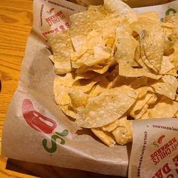Chili's - Chips and salsa - A basket of tortilla chips served on branded paper with a small bowl of salsa on a wooden table. - Bars Near Me - Round Lake Beach, Illinois