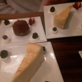 Patsy’s Pizzeria - 12/16/25 - Three dessert plates featuring a chocolate cake, cheesecake, and fruit garnishes are arranged on a dark wooden table. - Italian Near Me - Bronxville, New York