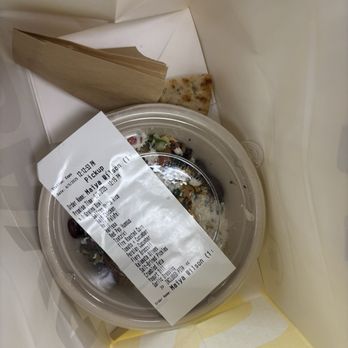 CAVA - The image shows a takeout meal inside a paper bag, including a plastic container with a salad, a piece of pita bread, and a paper bag. The receipt is placed on top of the salad container, displaying order details and pickup time. The items are arranged in a typical takeout presentation, with the salad and pita bread visible for easy access. - Salad Near Me - Coppell, Texas