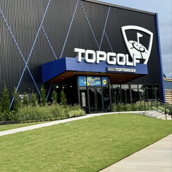 Topgolf - Exterior view of Topgolf, a golf entertainment venue, featuring a large sign, modern black building facade, and landscaped surroundings. - Sports Bars Near Me - Mobile, Alabama