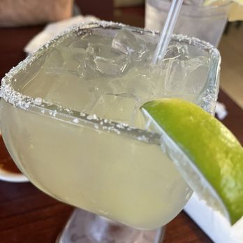 El Comal - Margarita - A margarita cocktail with ice, a salted rim, and a lime wedge is served in a large glass at a restaurant table. - Mexican Near Me - Santa Fe, New Mexico