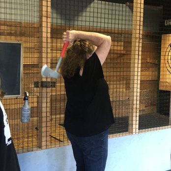 Oregon Axe - Learning to throw an axe - A woman with curly hair is preparing to throw an axe at an indoor axe throwing lane, with a wooden and wire mesh background. - Axe Throwing Near Me - Springfield, Oregon