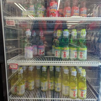 Daiso - Many Ramune flavors to choose from - A refrigerated display case contains multiple bottles of Ramune flavored drinks, including strawberry, melon, and lemon varieties, arranged on several shelves. - Department Stores Near Me - Austin, Texas