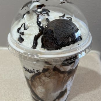 Better Together Cafe - Cookies n' Cream Shake - A cookies and cream milkshake in a clear plastic cup with a dome lid, topped with whipped cream, Oreo cookies, and drizzled with chocolate syrup. The drink has a swirled appearance with visible Oreo pieces and chocolate streaks throughout. - Desserts Near Me - South Milwaukee, Wisconsin