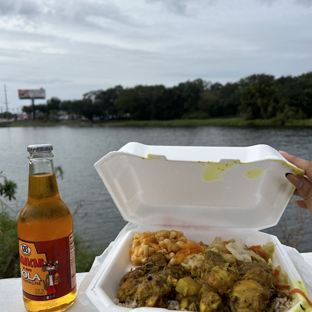 A Kola champagne, curry chicken, rice and peas, steamed cabbage, a water view