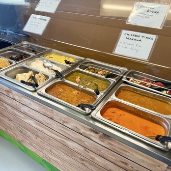 Nanglo Momos & Curry - A buffet with various Indian dishes in stainless steel trays, labeled with signs indicating chicken bhuna, chicken tikka masala, and dal makhani. - Himalayan/Nepalese Near Me - Appleton, Wisconsin