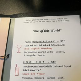 The image shows a printed menu page with a list of cocktails, including 'Mars-capone Attacks!' and 'M.O.G.U.E.R.A.', each with descriptions and prices. The menu features illustrations of a wine glass and a cocktail glass in red ink. The page includes a note about food allergies and is placed on a dark surface, possibly inside a restaurant or bar setting.