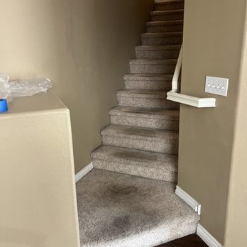 Divinity Flooring Services - Stairs before - A carpeted staircase with multiple steps, showing a dark stain on the bottom step and a stained carpet at the base, located in an indoor setting. - Flooring Near Me