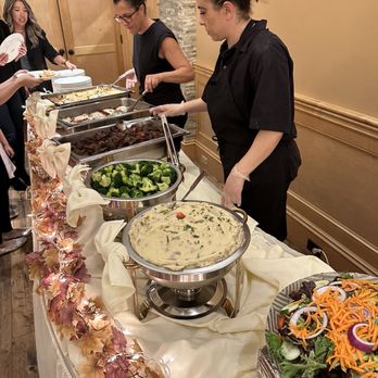 Avellino's Restaurant & Catering - Two staff members are serving food from chafing dishes at a buffet in a restaurant, with a salad and vegetable dishes visible. - Italian Near Me - Medford, Massachusetts